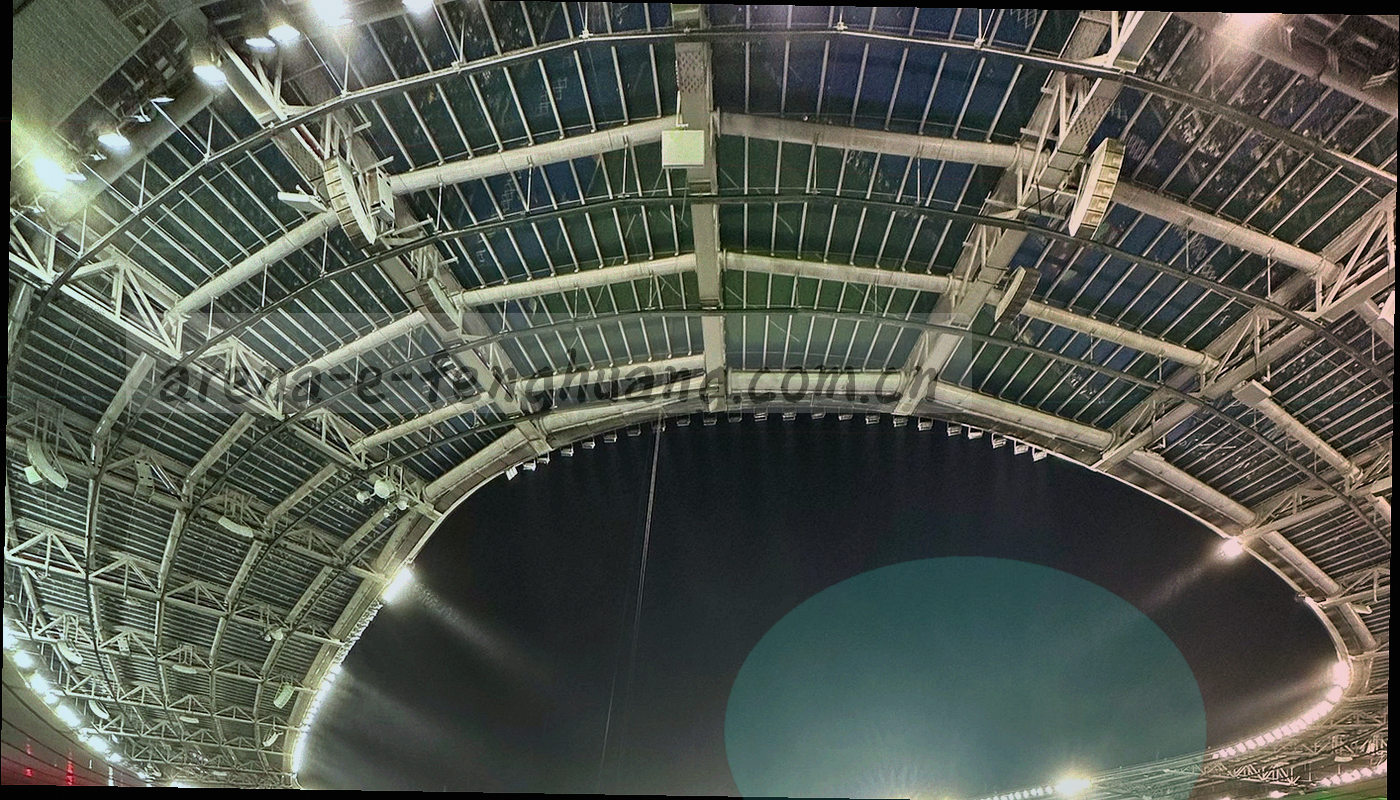 夜间球场灯光下比赛正在进行的远景画面，运动员以背影出现